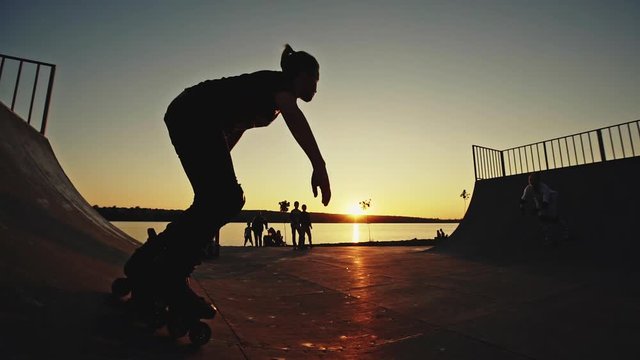 Silhouette roller skate in the roller park, two teenagers perform complex jumps against the background of the sunset.