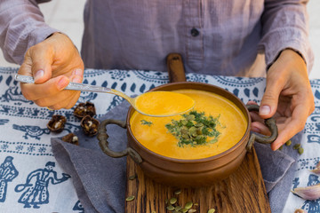 Woman hands holds pumpkin curry creamy soup with coconut milk, parsley. Sweet orange hot pumpkin soup in vintage pot or bowl.