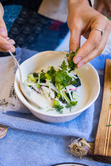 Woman hands holds okroshka - a cold soup made from cucumber, kvass, radish, dill, parsley. Vegan raw okroshka with coconut milk yoghurt, lemon, garlic. Vegetarian lunch or dinner. Healthy food.