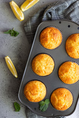 Homemade lemon muffins in black teflon baking dish over grey concrete background. Copy space.