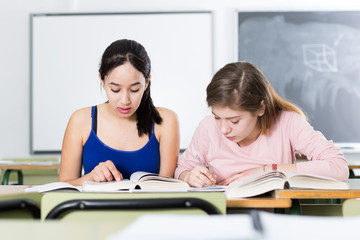 Young girls are sitting at the desk and reading text in the classroom