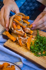 Traditional autumn  baked pumpkin. Woman hands holds squash fried sticks with onion, olive oil, herbs, paprika in a parchment paper cone.  Vegan lunch, vegetarian dinner, healthy food.