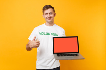 Man in white t-shirt written inscription green title volunteer hold laptop pc computer with blank empty screen isolated on yellow background. Voluntary free assistance help, charity grace work concept