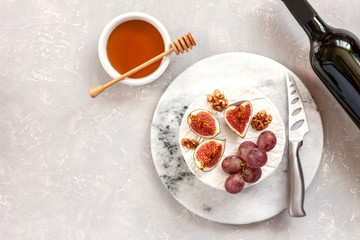 Fresh soft brie cheese with honey, walnuts, figs, grapes and bottle of red wine. Top view, close-up on gray concrete background.