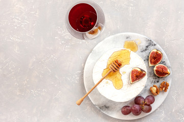 Fresh soft brie cheese with honey, walnuts, figs, grapes and glass of red wine. Top view, close-up on gray concrete background.