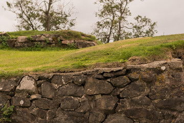Anciend wall made of huge black stones with grass on its top. Korela Fortress, Russia