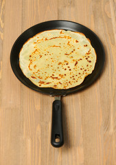 Crepe closeup, thin pancake on a frying pan, wooden background