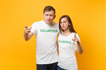 Portrait of young colleagues couple in white t-shirt with written inscription green title volunteer isolated on yellow background. Voluntary free work, assistance help, charity grace teamwork concept.