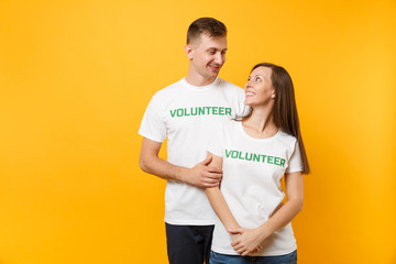 Fototapeta premium Portrait of young colleagues couple in white t-shirt with written inscription green title volunteer isolated on yellow background. Voluntary free work, assistance help, charity grace teamwork concept.