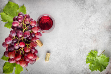 Ripe grape bunch  with leaves and glass of wine on stone background. Top view with copy space