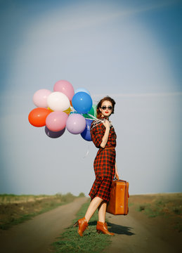 Beautiful girl in plaid dress with multicolored balloons and bag on countryside