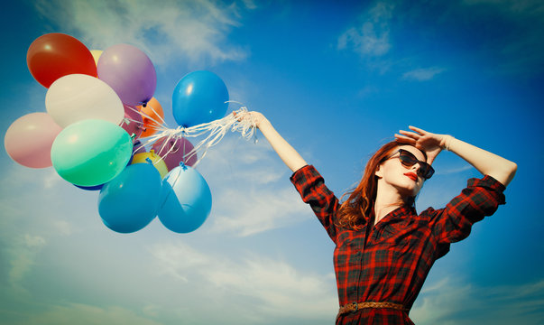 Beautiful girl in plaid dress with multicolored balloons on blue sky background