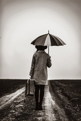 portrait of a young beautiful woman with umbrella and brown suitcase standing on the road. Image in black and white color style