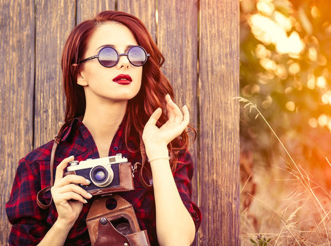 Beautiful girl in plaid dress with camera and sunglasses on wooden background.