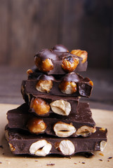 Broken dark chocolate with hazelnuts on wooden background.