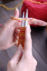 Women's hands knit on the needles of yellow and red yarn.