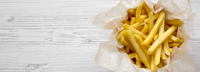 French fries in paper box over white wooden background, top view. Copy space.