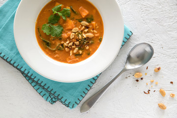 Peanut stew in white bowl with spoon and blue napkin