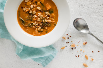 Peanut stew in white bowl with spoon and napkin