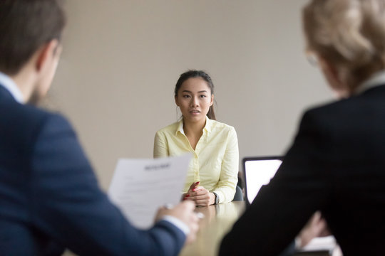 Back view of recruiters interview young Asian job candidate asking questions, reading her resume, hr managers hiring employee, considering cv experience, worried intern talk at recruitment process