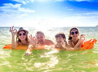 Happy family of four in vacation at sea shore. Happy family with yellow mattress bathes in sea. happy mum daddy and two children play in water