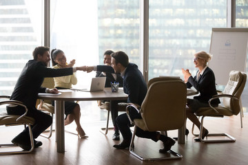 Excited male employees give fists bump celebrating successful contract closing during meeting,...