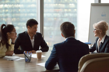 Diverse employees talk at briefing discussing company plans and projects, middle aged businesswoman...