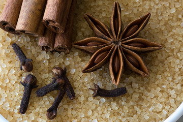 Anise star, cloves and cinnamon rolls spices on brown cane sugar background. Close up.