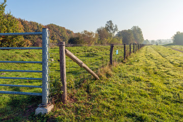 Rural landscape with an iron gate and a fence of mesh and wooden poles