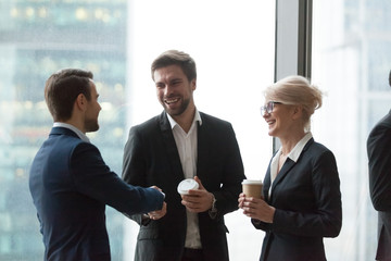 Smiling office workers talk having casual conversation, get acquainted during meeting, excited colleagues handshaking introducing at coffee break at briefing, happy workers greeting shaking hands