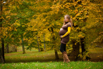 Beautiful pregnant woman outdoor in park on autumn afternoon with vibrant nature colors in background