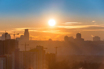 Panoramic view of sunset in the city with silhouette of buildings and industrial cranes