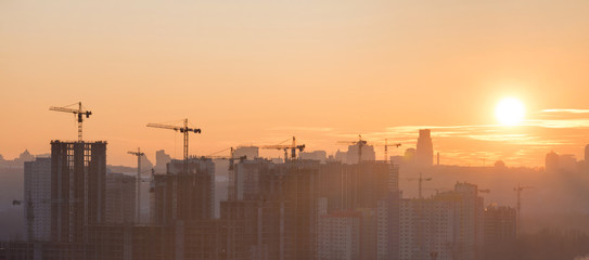 Panorama of sunset in the city with silhouette of buildings and industrial cranes
