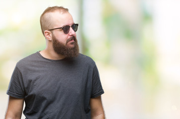 Young caucasian hipster man wearing sunglasses over isolated background looking away to side with smile on face, natural expression. Laughing confident.
