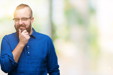 Young caucasian hipster man wearing glasses over isolated background looking confident at the camera with smile with crossed arms and hand raised on chin. Thinking positive.
