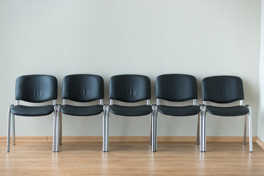 Row Of Black Office Chairs Standing In Corridor Or Conference Room, Empty Dark Seats Arranged In Line In Boardroom, Range Of Basic Stools In Front Of White Wall. Interview, Recruitment Concept