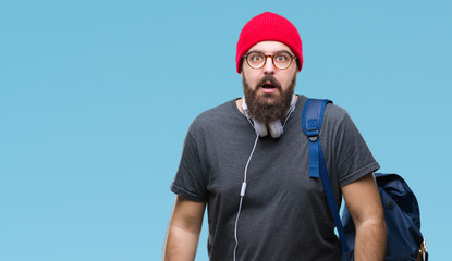 Young hipster man wearing red wool cap and backpack over isolated background afraid and shocked with surprise expression, fear and excited face.