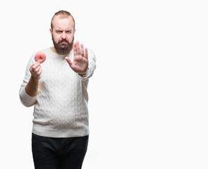 Young caucasian hipster man eating sweet donut over isolated background with open hand doing stop sign with serious and confident expression, defense gesture