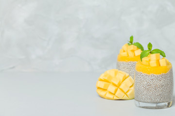 Chia seeds pudding with mango puree in beautiful glasses with green mint leaves and cut fresh ripe tropical fruit.