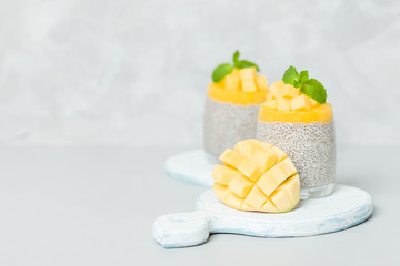 Chia seeds pudding with mango puree in beautiful glasses with green mint leaves and cut fresh ripe tropical fruit.
