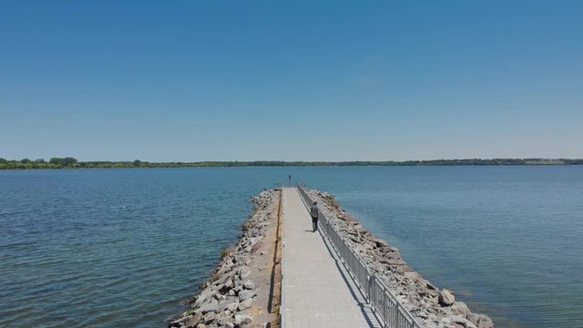 Aerial Pier Toward End and Over Water. an aerial flyover a lake pier while someone walks toward the end