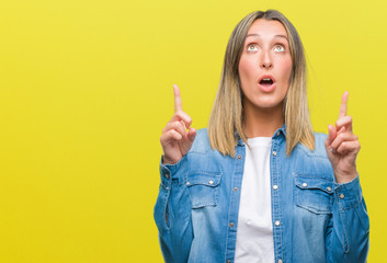 Young beautiful woman over isolated background amazed and surprised looking up and pointing with fingers and raised arms.
