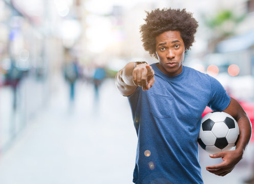Afro american man holding football ball over isolated background pointing with finger to the camera and to you, hand sign, positive and confident gesture from the front