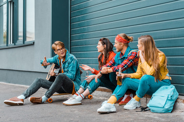 Fototapeta premium hipsters drinking beer together on street while man playing acoustic guitar