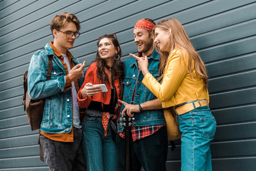 happy young hipsters using smartphone together on street