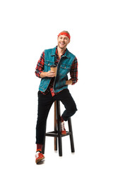 cheerful man in headband and denim vest sitting on chair with coffee cup isolated on white