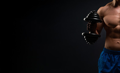 Handsome power athletic man in training swap muscles with dumbbells. A strong six-pack bodybuilder, perfect abs, shoulders, biceps, triceps and chest. On a dark background under the banner