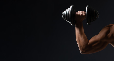 Fototapeta na wymiar Sports wallpaper on a dark background. A strong hand with dumbbells. The space for advertising, sports nutrition, slim body, an athlete and a strong man