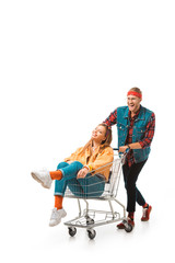 Plakat happy young man carrying shopping trolley with girlfriend isolated on white