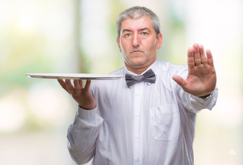 Handsome senior waiter man holding silver tray over isolated background with open hand doing stop...